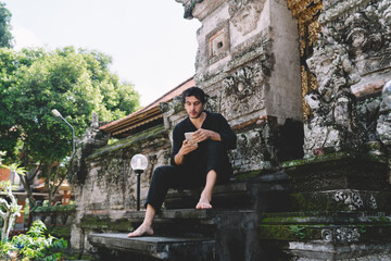 Serious ethnic man browsing smartphone on stairs