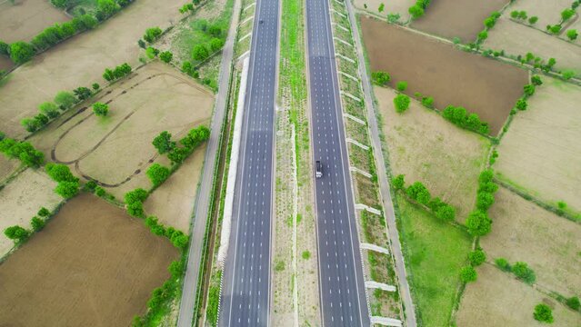 aerial drone shot pan up revealing delhi mumbai surat vadodra high going off into distance with green feilds and cloudy skies showing the rapid pace of Indian road construction