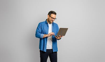Confident male entrepreneur analyzing report over laptop while standing over white background - Powered by Adobe