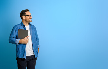 Thoughtful smiling businessman holding digital tablet and looking away against blue background