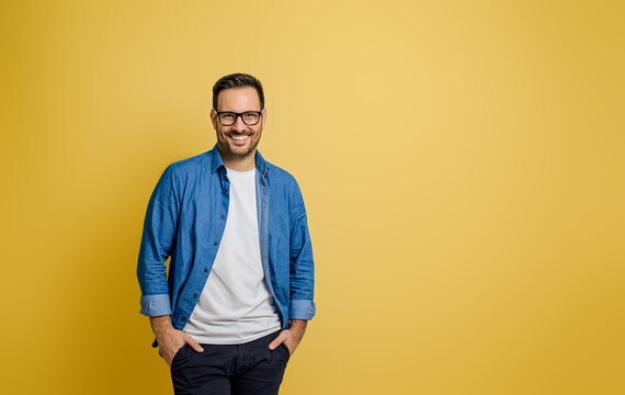 Portrait of smiling confident male entrepreneur with hands in pockets posing on yellow background