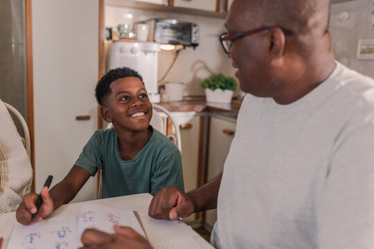 menino Brasileiro sentado na cozinha sorrindo para o seu pai que o est&aacute; ajudando na tarefa de casa no Brasil