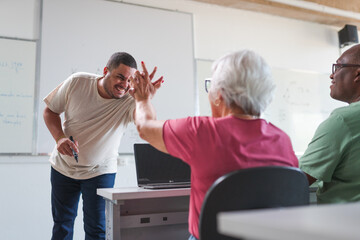 Brazilian teacher celebrates by giving high five to his elderly female student during an ongoing adult class at a school in Brazil
