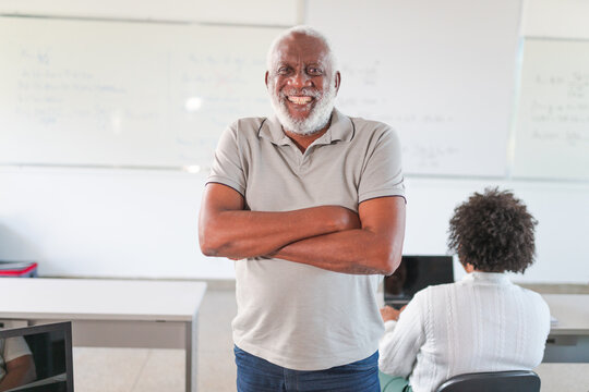 retrato de um homem negro Brasileiro de cabelos e barba brancos sorrindo de braços cruzados na sala de aula em um curso para adultos no Brasil