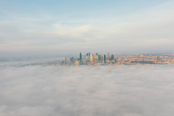 Drone flies towards the urban landscape with buildings in the fog at sunrise. Aerial view of cityscape in the fog at sunrise. Warsaw Poland.