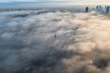 Drone flies towards the urban landscape with buildings in the fog at sunrise. Aerial view of cityscape in the fog at sunrise. Warsaw Poland.