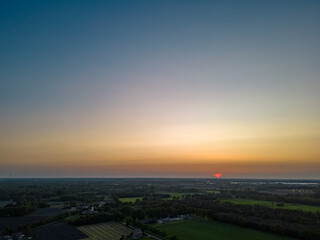Aerial view of endless lush pastures and farmlands of Belgium under a colorful and dramatic sunset sky. Beautiful Irish countryside with emerald green fields and meadows. Rural landscape on sunset