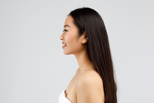 Profile portrait of happy beautiful asian woman with perfect skin and thick hair smiling, posing on grey background