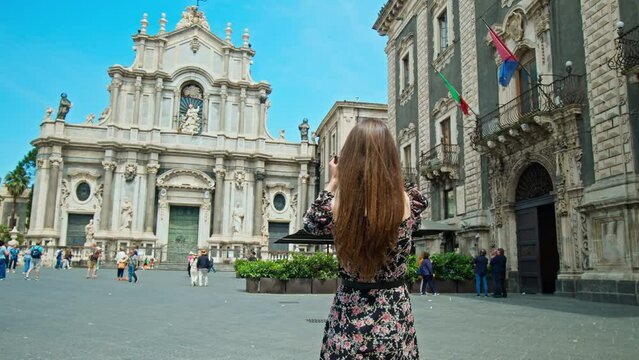 A beautiful woman takes pictures of Basilica Cattedrale di Sant'Agata in Catania, Italy. Fashionable Girl takes photos of the prominent baroque cathedral with its columned facade, domed roof, frescoes