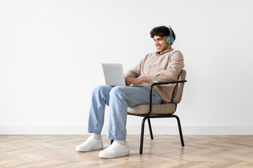 Arabic Guy Using Laptop Surfing Web Wearing Headphones Sitting Indoor