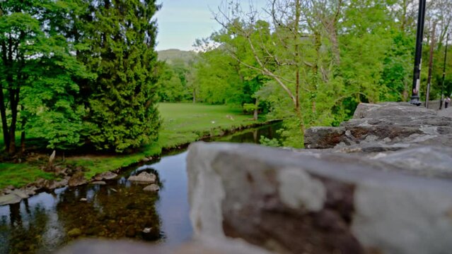 Rack focus from a stone wall to the River Conwy with a field and trees in the village of Betws-y-Coed in Snowdonia National Park, Wales, UK