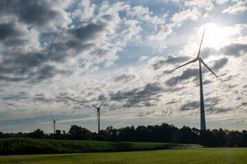 Silhouettes of wind turbines on a green agrarian farm field against dramatic clouds before the...
