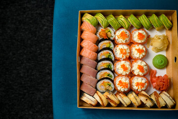 Top view on different sushi rolls with salmon, avocado and smocked eel on blue sofa on black carpet