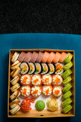 Top view on different sushi rolls with salmon, avocado ,smocked eel in delivery box on blue sofa on black carpet