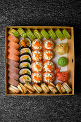 Top view on different sushi rolls with salmon, avocado, smocked eel in delivery box on black background