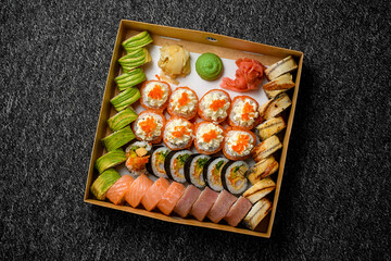 Different sushi rolls with salmon, avocado, smocked eel, tobiko caviar in delivery box on black background