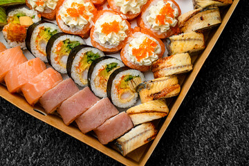 Closeup view on different sushi rolls with salmon, avocado, smocked eel, tobiko caviar in delivery box on black background