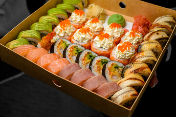 Set of sushi rolls with salmon, avocado, smocked eel, tobiko caviar in transport box in woman's hand