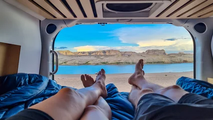 Fotobehang Camps Bay Beach, Kaapstad, Zuid-Afrika Legs of couple lying in camper van with panoramic sunset view of Wahweap Bay at Lake Powell, Glen Canyon Recreation Area, Page, Utah, USA. Sand beach on wild campground. Road trip romantic atmosphere