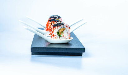 Sushi rolls in a white ceramic spoon on a black bamboo plate. Japanese food, eating healthy