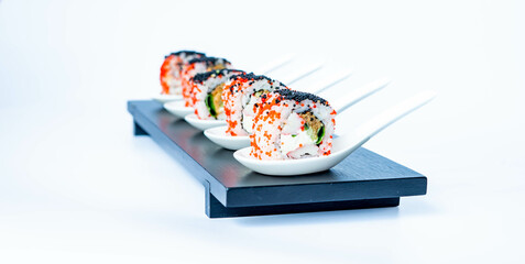 Sushi rolls in a white ceramic spoon on a black bamboo plate. Japanese food, eating healthy