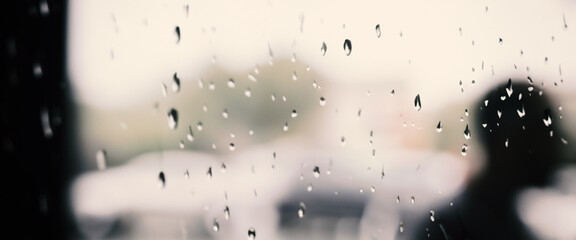 Rain drop on window glass of coffee shop and blurry city life background. Rainy season and blurry people city day life or bokeh night lights outside window. Coffee shop window covered with rain water