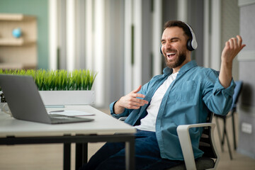 Cheerful young businessman having fun at workplace in office, playing virtual guitar