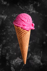 Pink ice cream in a waffle cone on a dark background