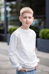 Stylish school boy in white hoodie walking on street in city. Mock up children clothes.