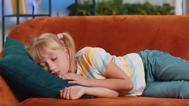 Tired preteen school girl lying down in bed taking a rest at home on couch. Carefree blonde child kid napping, falling asleep on comfortable sofa with pillows. Closed her eyes enjoy daytime nap alone