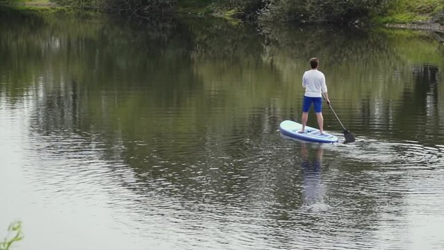 caucasian man on sup board. a man with glasses stands and rows with an oar on the sup board. a man swims to the other side of the pond. slow motion video. High quality Full HD video recording
