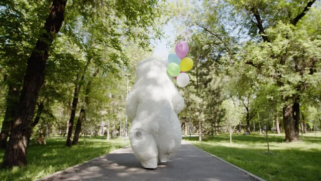 A giant polar bear puppet doll dances with balloons in a green park, in a background of green trees, in summer, outdoors. The concept of recreation, children's party