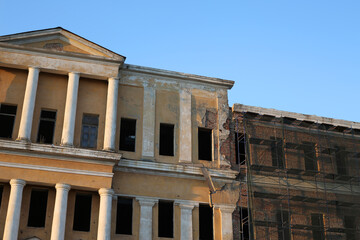 Fototapeta premium Abandoned building under renovation. An old windowless building with a yellow façade and scaffolding for workers. Exterior of an old shabby building