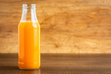 A glass bottle of fruit juice. Orange  juice on wooden table.