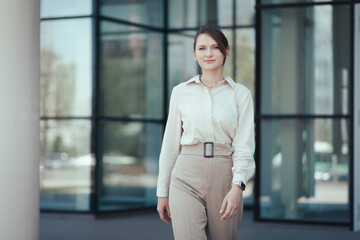 Successful caucasian business woman in a fashionable business suit comes out of a modern business building, looks at the camera.