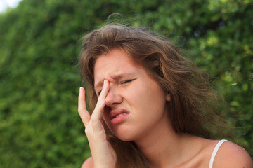 Young woman scratching itchy and rub eyes with her hands in a park, problems with vision, allergy...