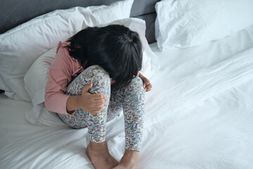 a sad child girl cover her face with hand sitting on bed 