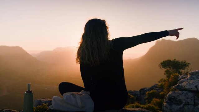 A Young woman sitting on mountain at sunset pointing to the right, Eagles Nest, Constatia, Cape Town