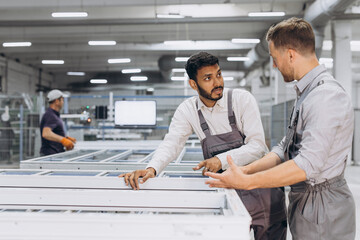 Two male international workers in overalls work together at a machine for the production of...
