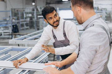 Two male international workers in overalls work together at a machine for the production of...