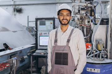 Operator of machine. Industrial worker indoors in factory. Young technician in white hard hat.