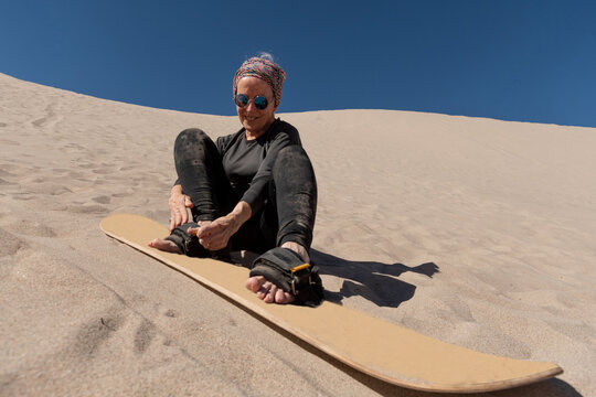 70-year-old woman putting on a sandboard to slide on the sand