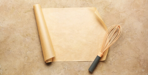 Roll of baking paper and whisk on beige background