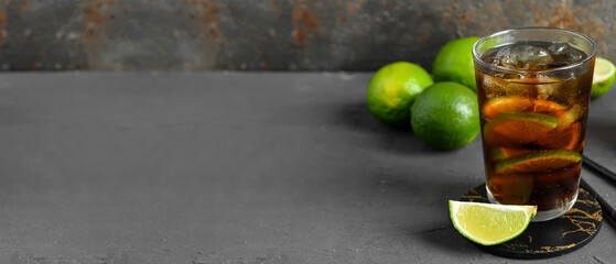 Glass of cold Cuba Libre cocktail on dark grunge background with space for text
