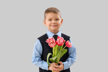 Cute little boy in suit with tulips on grey background