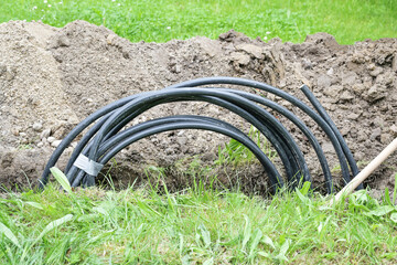 Coiled black power cable in a narrow ditch in the lawn to install a house connection, energy...