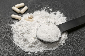 Scoop of amino acid supplements on dark background, closeup