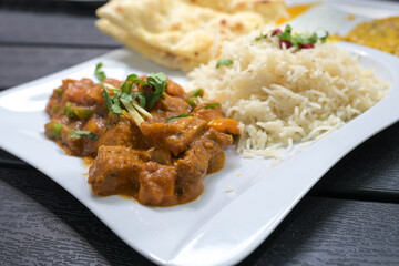 Indian meal, beef with vegetables in a spicy sauce, rice and bread on a white plate and a black table, selected focus