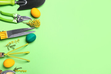 Gardener's tools with Easter eggs and flowers on green background