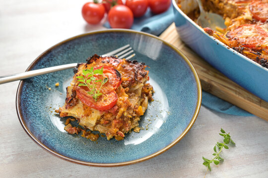 Lasagna portion in a blue plate, casserole dish with pasta layers, Bolognese sauce, ground beef, vegetables and tomatoes, topped with melted cheese, copy space, selected focus